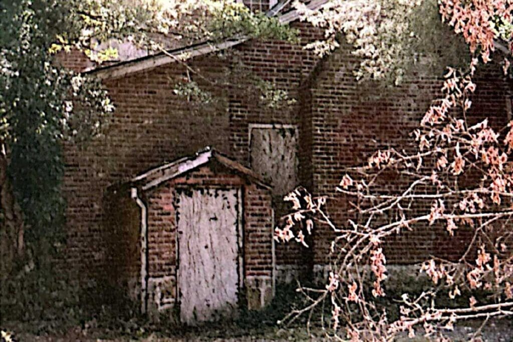 A 1960s view of the Bradford-Berry House, showing weathered red brick and a small boarded entry porch behind autumn branches.