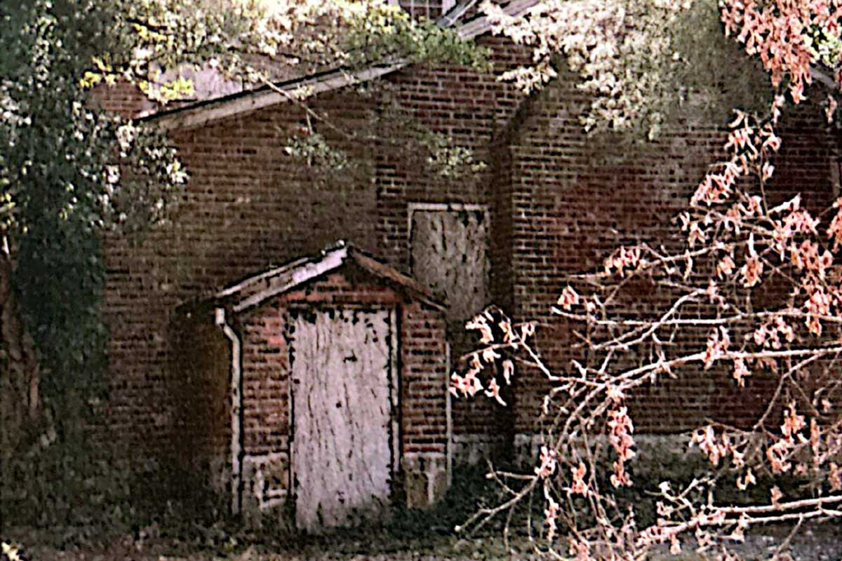 A 1960s view of the Bradford-Berry House, showing weathered red brick and a small boarded entry porch behind autumn branches.