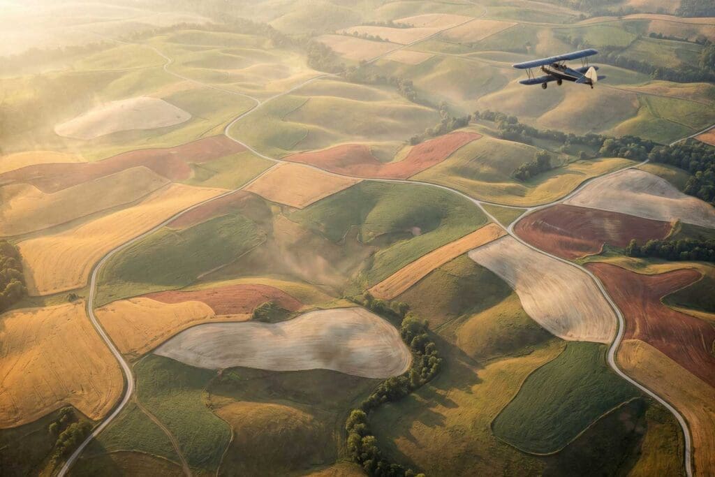 Vintage blue biplane flying over the rolling patchwork farmland of Sumner County, Tennessee at golden hour